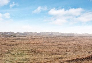 Panoramisch beeld van vakantiehuisjes in Pandrup, Denemarken, omringd door velden en blauwe lucht.