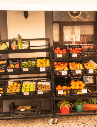 Verse groente- en fruitrekken buiten een winkel met kleurrijke producten en planten in potten.