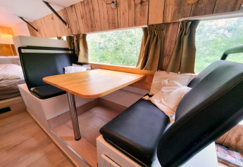 Interieur van de REEBUS camper in België met een eethoek, houten panelen en groene gordijnen.