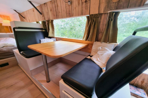 Indvendig udsigt over REEBUS mobilhome i Belgien med spiseområde, træpaneler og grønne gardiner.