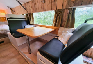 Indvendig udsigt over REEBUS mobilhome i Belgien med spiseområde, træpaneler og grønne gardiner.