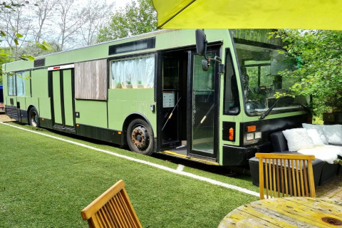 Et billede af en grøn mobilhome-bus kaldet 'REEBUS' i Belgien, omgivet af have og havemøbler.