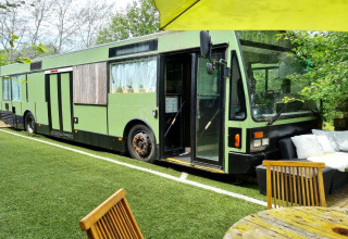 Et billede af en grøn mobilhome-bus kaldet 'REEBUS' i Belgien, omgivet af have og havemøbler.