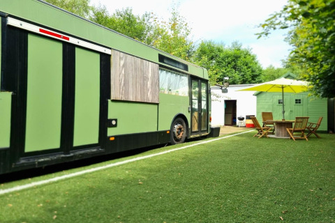 Et grønt mobilhome kaldet 'REEBUS' i Belgien, med udendørs siddepladser og kunstgræs.
