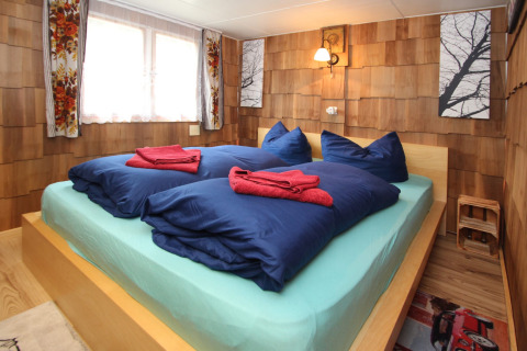 Bedroom in Holiday home «Susanne 58 qm» with double bed, blue bedding, and wood-paneled walls in Germany.