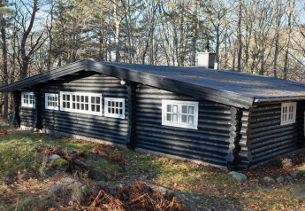 Chalet en rondins noir aux fenêtres blanches entouré d’arbres à Frederiksværk, Danemark.