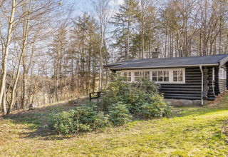 Schwarze Blockhütte inmitten von Bäumen und Sträuchern bei Tageslicht in Frederiksværk, Dänemark.