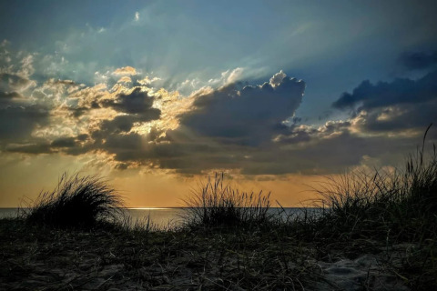 Zonsondergang op het strand in Frederiksværk, Denemarken, met gras en dramatische wolken boven zee.