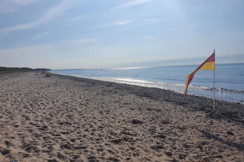 Sandstrand in Frederiksværk, Dänemark mit rotem und gelbem Flagge am Meer an einem sonnigen Tag.