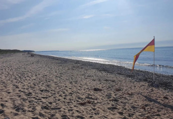 Spiaggia soleggiata a Frederiksværk, Danimarca con sabbia, ciottoli e una bandiera rosso-gialla vicino al mare.