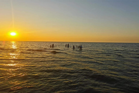 Zonsondergang boven zee met badende mensen nabij het 4-persoons vakantiehuis in Frederiksværk, Denemarken.
