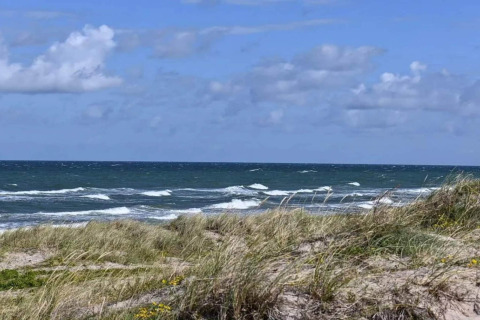 Vista su dune di sabbia e onde del mare sotto un cielo azzurro da una casa vacanze a Frederiksværk, Danimarca.