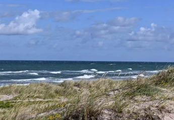Vue sur des dunes de sable et les vagues sous un ciel bleu depuis une maison de vacances à Frederiksværk, Danemark.
