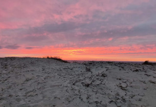 Zonsondergang boven zandduinen vanaf een vakantiehuis in Frederiksværk, Denemarken, met roze lucht.