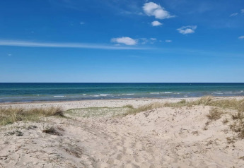 Vista de la playa y el mar en Frederiksværk con dunas y cielo azul, desde una casa de vacaciones en Dinamarca.