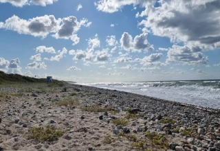 Stenstrand og sand ved Frederiksværk i Danmark, med blå himmel og spredte skyer over havet.
