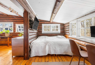 Dormitorio acogedor en cabaña de troncos con techo blanco, suelo de madera, escritorio y ventanas en Frederiksværk.
