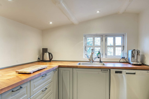 Moderne keuken met houten aanrecht, waterkoker, broodrooster en vaatwasser in Frederiksværk vakantiehuis.