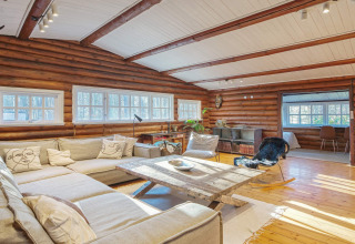 Helles, geräumiges Wohnzimmer in einer Blockhütte mit großen Fenstern, Holzwänden und gemütlichem Sofa.