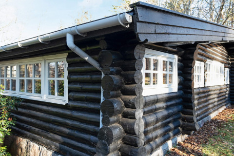 Sort bjælkehytte med hvide vinduer ved 4 personers feriehus i Frederiksværk, Danmark, omgivet af natur.