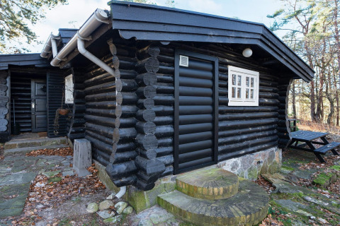 Zwart geschilderde blokhut met wit raam en stenen treden in het bos bij Frederiksværk, Denemarken.