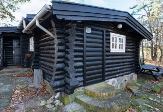 Zwart geschilderde blokhut met wit raam en stenen treden in het bos bij Frederiksværk, Denemarken.
