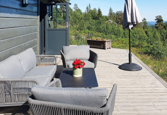 Outdoor terrace at a chalet in Sweden with gray patio furniture, a sun umbrella, and scenic nature views.