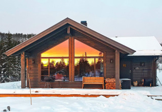 Chalet pour 6 personnes à Passebekk, Suède, enneigé, reflet du coucher de soleil dans les fenêtres.