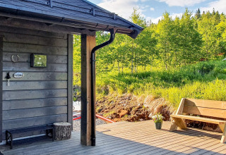 Terrasse en bois d’un chalet de vacances à Passebekk, Suède, avec banc et vue sur la forêt verdoyante.
