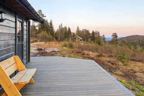 Terrazza in legno e panchina al chalet '6 person holiday home in Passebekk' in Svezia, vista su colline e pini.