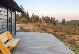 Holzterrasse und Bank bei Chalet '6 person holiday home in Passebekk' in Schweden mit Blick auf bewaldete Hügel.