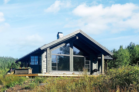 Modern houten chalet met grote ramen en een terras, gelegen tussen de natuur in Passebekk, Zweden.