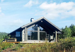 Moderne træchalet med store vinduer og overdækket terrasse omgivet af natur i Passebekk, Sverige.