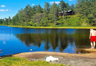 Homme en short rouge près du lac devant le chalet 6 person holiday home in Passebekk, entouré de forêt en Suède.