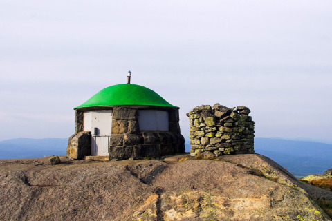 Pequeña cabaña de piedra con techo verde en la cima rocosa de una montaña en Suecia junto a un círculo de piedras.