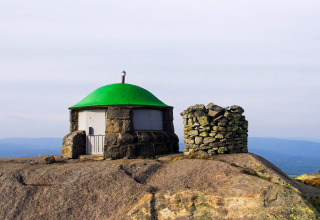 Pequeña cabaña de piedra con techo verde en la cima rocosa de una montaña en Suecia junto a un círculo de piedras.