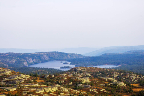 Zicht vanuit een chalet in Passebekk, Zweden, met een meer, bossen en rotsachtige heuvels in de verte.