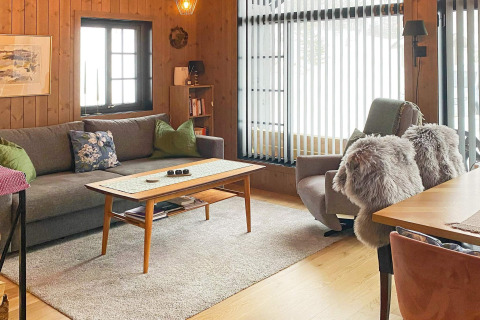 Soggiorno accogliente in uno chalet svedese con pareti in legno, divano, poltrona e ampie finestre.