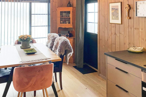 Et hyggeligt spiseområde i et træbeklædt sommerhus med moderne køkken, dækket bord og naturudsigt.