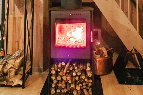 Poêle à bois avec feu allumé et bûches rangées, dans un chalet de vacances à Passebekk, Suède.