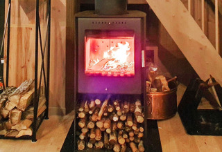 A cozy wood stove with burning firewood in a holiday chalet in Passebekk, Sweden, firewood stacked nearby.