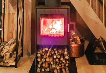 Poêle à bois avec feu allumé et bûches rangées, dans un chalet de vacances à Passebekk, Suède.