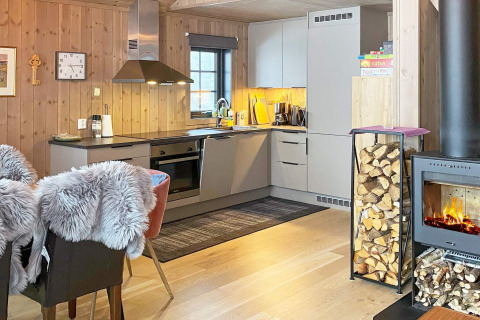 Modern chalet kitchen and living area with fireplace, wood storage, and fur-covered chairs. Passebekk, Sweden.