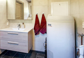 Badezimmer mit Waschbecken, Spiegelschrank, zwei roten Handtüchern und Boiler in einem Chalet in Passebekk, Schweden.