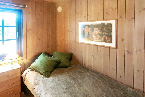 Schlafzimmer mit Holzverkleidung, Einzelbett mit grünen Kissen und Fenster im Chalet in Passebekk, Schweden.