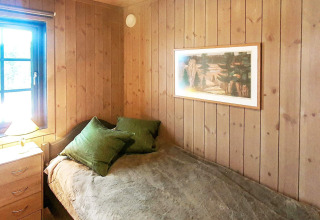 Slaapkamer met houten panelen, eenpersoonsbed, groene kussens en raam in chalet in Passebekk, Zweden.