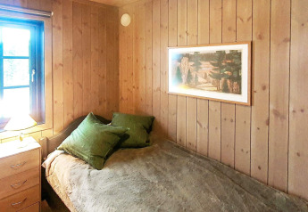 Dormitorio con paredes de madera, cama individual, cojines verdes y ventana en chalet en Passebekk, Suecia.