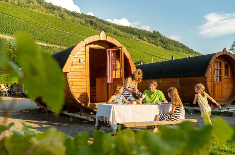 Famille dînant devant des cabanes tonneaux en bois au Camping Rissbach, entourée de vignes en Rhénanie-Palatinat.