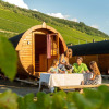Family dining outside unique wooden wine barrel cabins at Camping Rissbach, surrounded by vineyards in Rhineland-Palatinate.