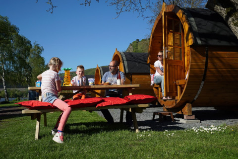 Family enjoys an outdoor meal by wooden barrel cabins at Camping Rissbach - Wijnvaten Rhineland-Palatinate glamping.